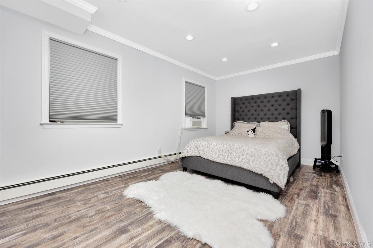 Bedroom with a baseboard heating unit, wood finished floors, recessed lighting, and crown molding