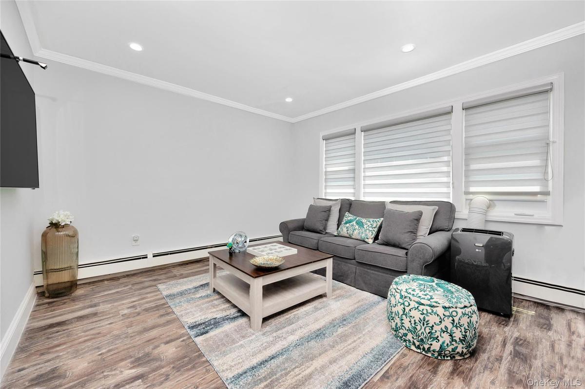Living area featuring a baseboard heating unit, wood finished floors, crown molding, and recessed lighting
