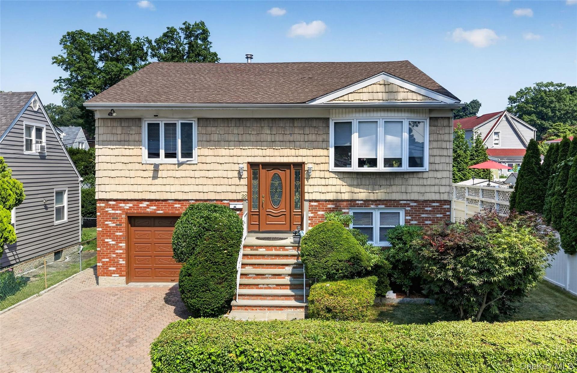 Split-level home featuring brick and shingle siding, an attached garage with a brown door, and a paver driveway
