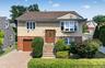Split-level home featuring brick and shingle siding, an attached garage with a brown door, and a paver driveway