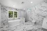 Spacious primary ensuite bathroom featuring large format marble-look tile flooring and walls, a freestanding soaking tub with floor-mounted faucet, a 