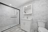 Main floor full modern bathroom featuring a frameless glass shower enclosure with matte black hardware, a white vanity with an integrated sink, an ill