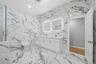 Primary ensuite bathroom featuring floor-to-ceiling white marble-look tile, a dual vanity with white cabinetry and integrated sinks, illuminated mirro