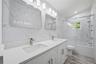 2nd floor full bathroom featuring a dual vanity with undermount sinks and brushed nickel faucets, a built-in bathtub with a sliding glass door, an ove