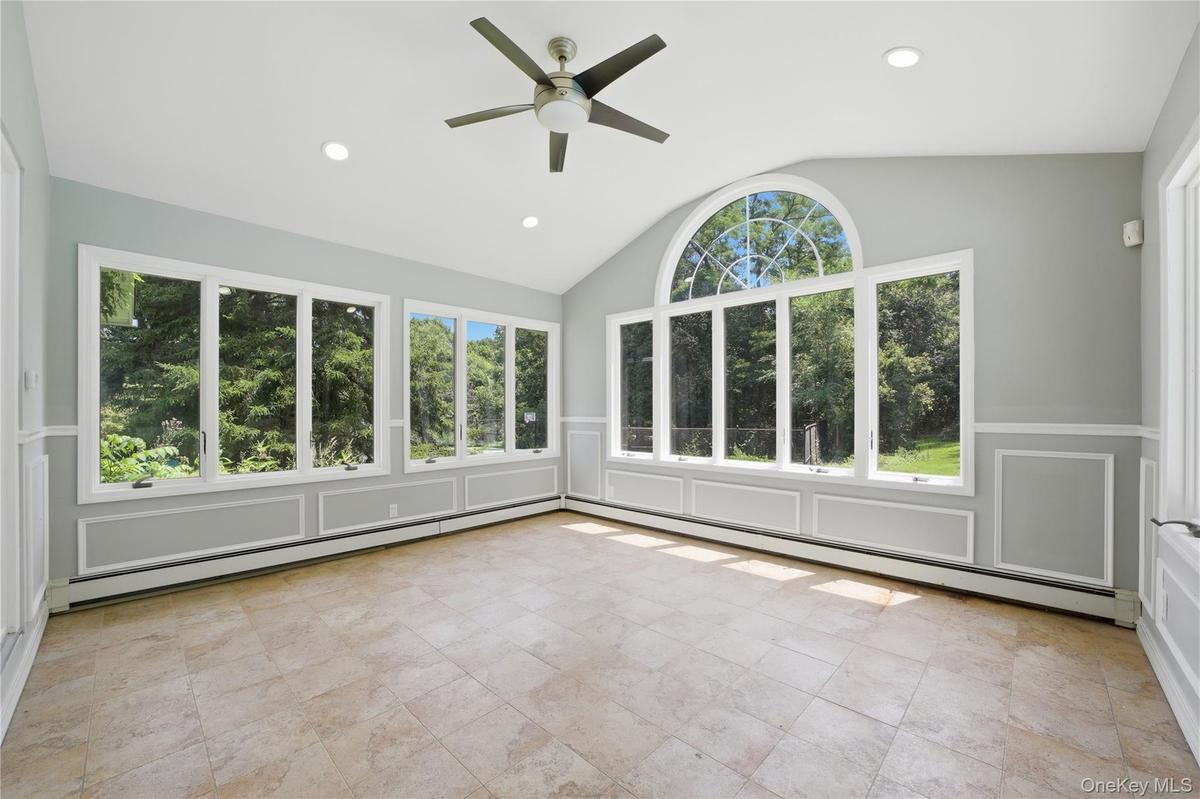 Light-filled room featuring large windows, a vaulted ceiling, recessed lighting, a ceiling fan, and tile flooring