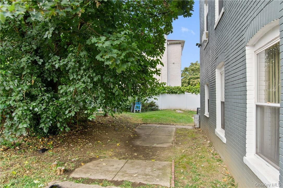 Side yard featuring a mature tree, concrete patio sections, and a privacy fence