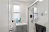 Bathroom featuring a single window, a vanity with a white countertop and gray cabinetry, and a shower enclosure with white subway tile
