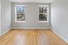 Room featuring natural wood flooring, two double-hung windows with blinds, light gray wall paint, and white baseboards