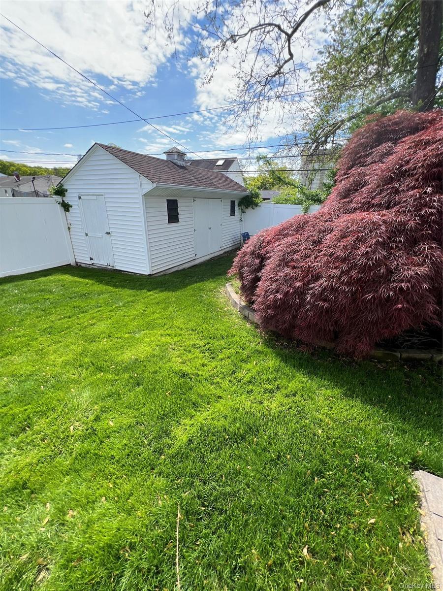 Expansive green lawn with a white vinyl fence and mature red-leafed tree
