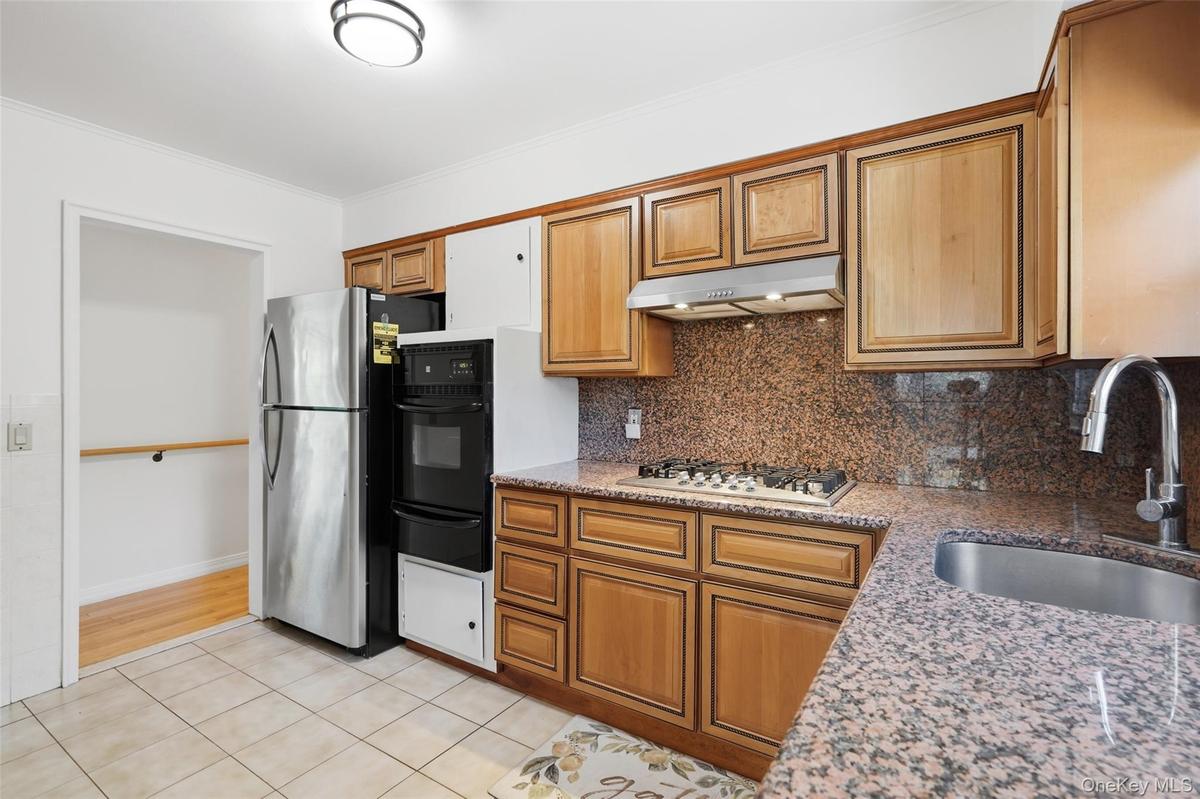 Kitchen featuring granite countertops and backsplash, wood cabinetry, stainless steel gas range, and an undermount sink with a gooseneck faucet