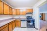 Kitchen featuring black gas range, stainless steel dishwasher, brown cabinetry, light stone counters, and under cabinet range hood