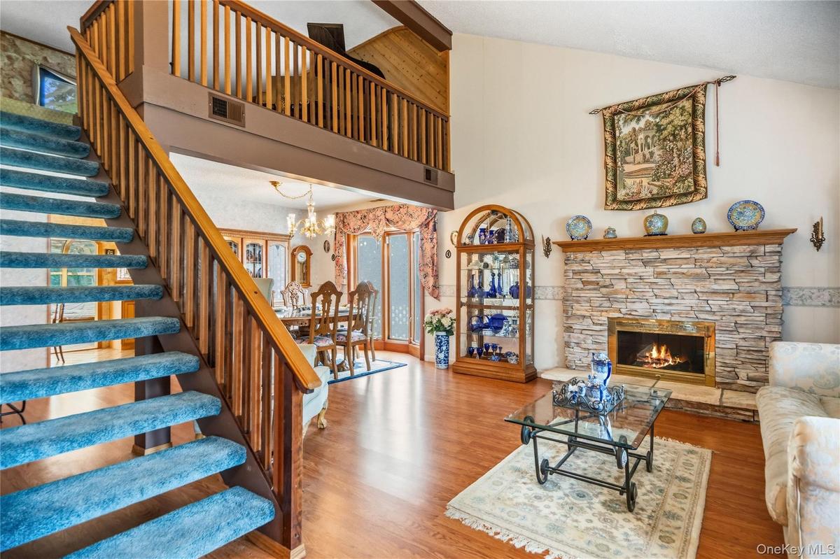 Open-concept living area featuring wood-finish, vinyl flooring, a two-story vaulted ceiling and a prominent staircase with wood railings leading to th