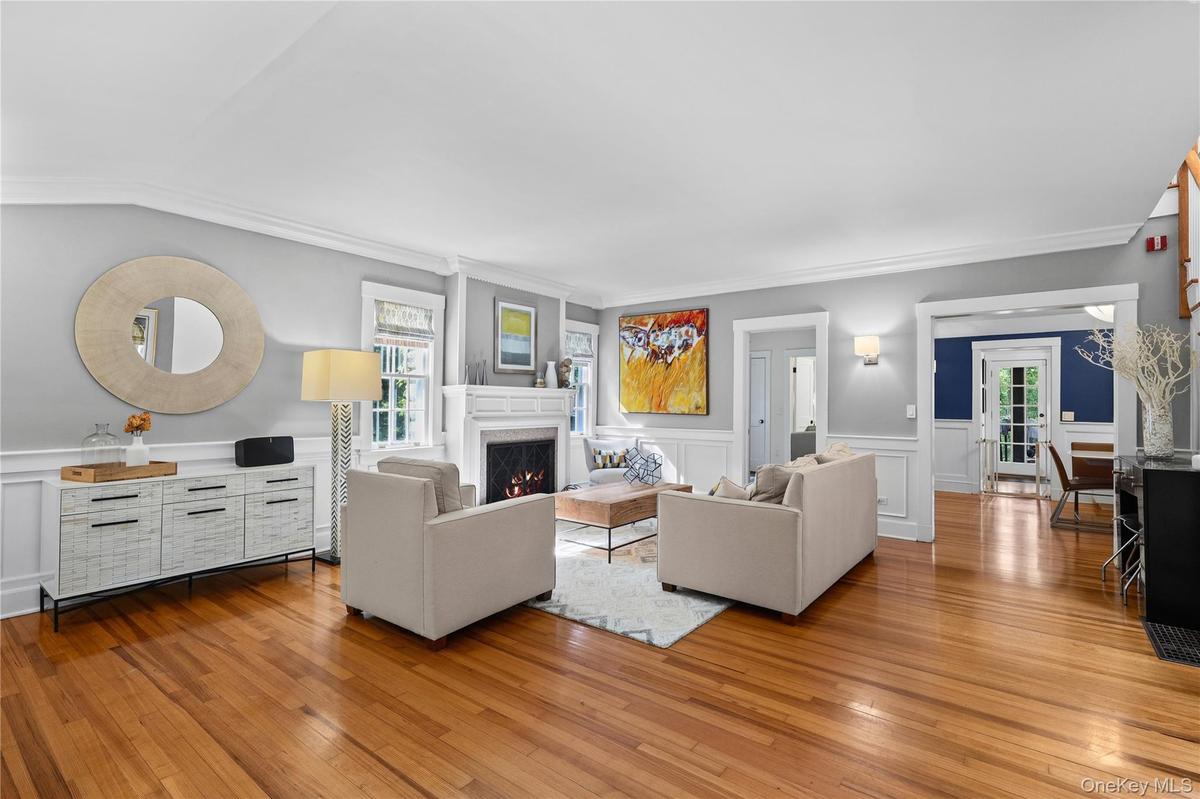 Spacious Living room featuring wood-finished flooring, white wainscoting, and a traditional fireplace.