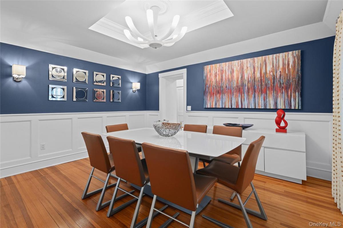 Dining room featuring wood-finish flooring, white wainscoting, and a tray ceiling.