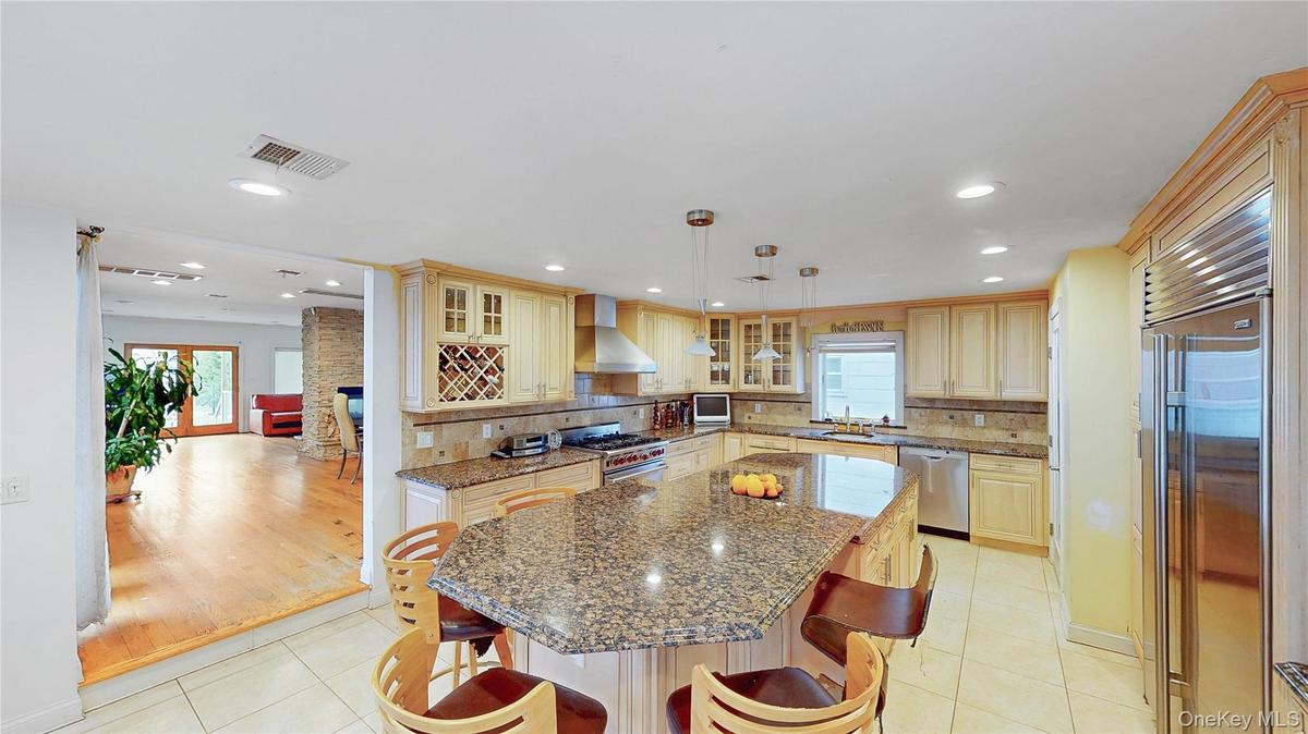 Spacious kitchen featuring an expansive island with a stone countertop, light wood-finish cabinetry, stainless steel appliances, and recessed lighting