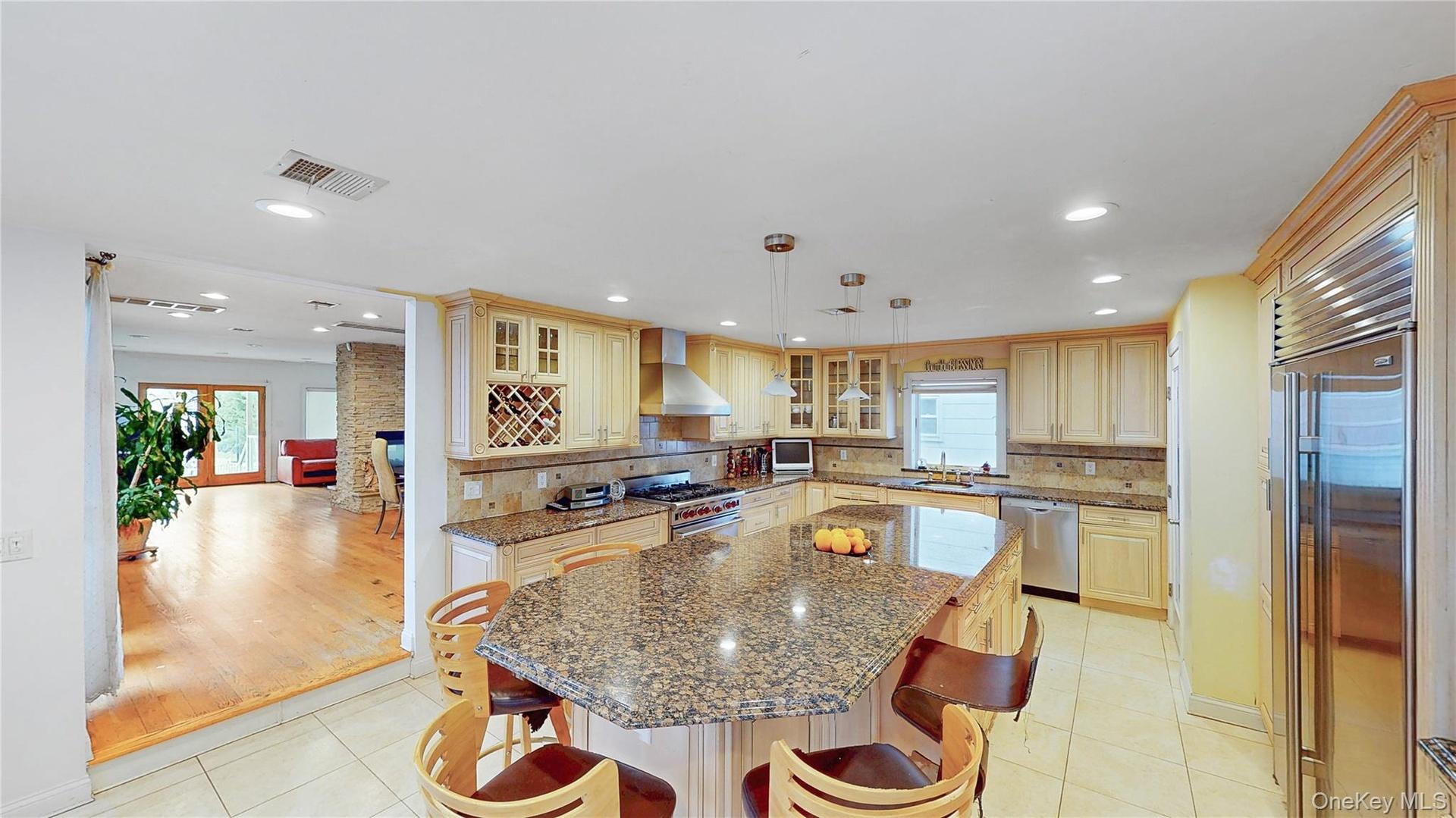 Spacious kitchen featuring an expansive island with a stone countertop, light wood-finish cabinetry, stainless steel appliances, and recessed lighting