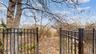 Wrought iron-style fencing with a gated entry, mature tree, and natural landscape