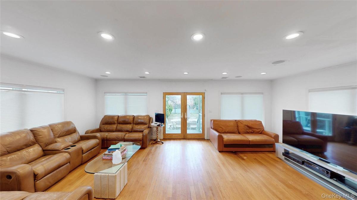 Spacious living area featuring light wood-finish flooring, recessed lighting, and multiple windows with blinds