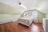 Attic room featuring rich wood-finish flooring, light green walls, two windows with white blinds, and a wall-mounted heating/cooling unit