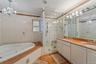 Bathroom featuring a built-in jetted tub, a glass-enclosed shower with a bench, and a dual-sink vanity with white cabinetry
