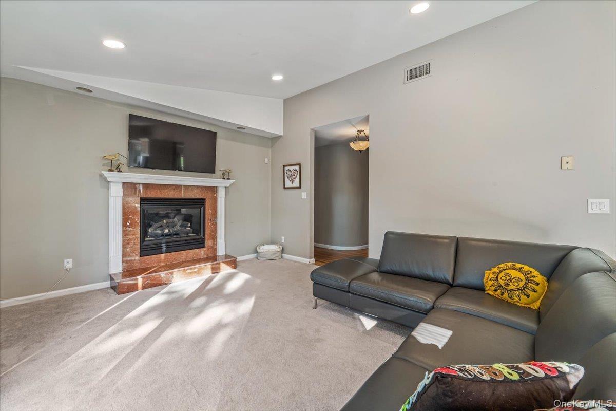 Living area featuring a fireplace with a stone-finish surround and white mantel, recessed lighting, carpet flooring, and a wall-mounted television