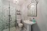 Glass-enclosed shower with subway tile surround, pedestal sink, and decorative wall mirror