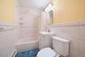 Bathroom featuring a full tub with shower, white tile surround, vanity with sink, and toilet