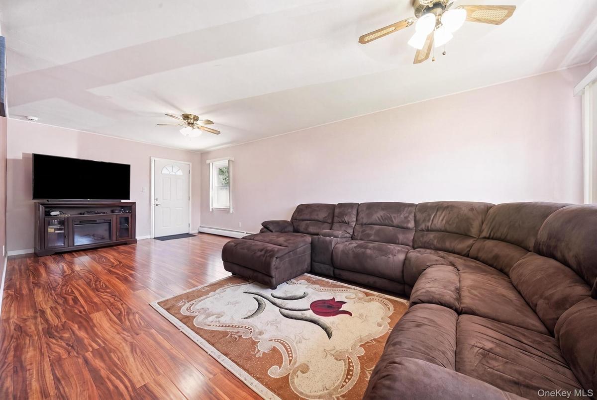 Spacious living area featuring wood-finish flooring, a ceiling fan, and a white entry door with frosted glass accents