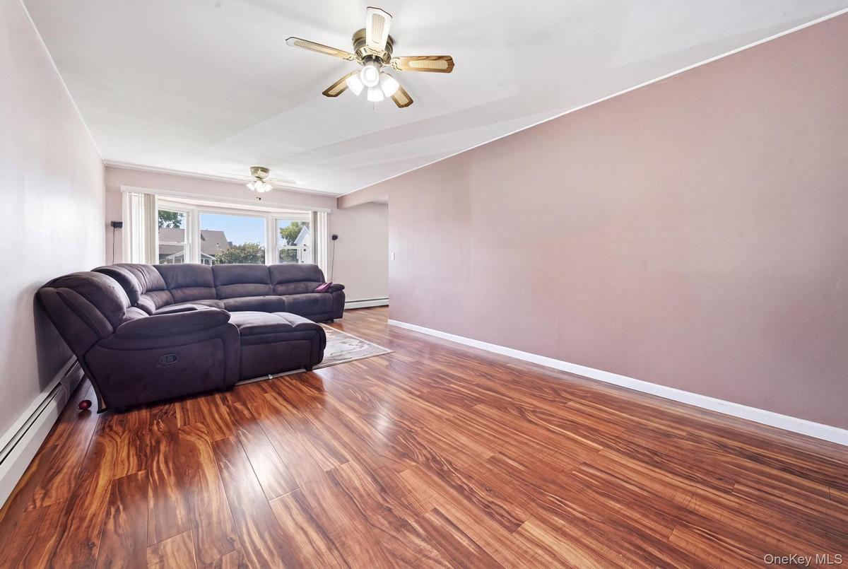Spacious interior featuring wood-finish flooring, a ceiling fan with integrated lighting, and a bay window providing natural illumination