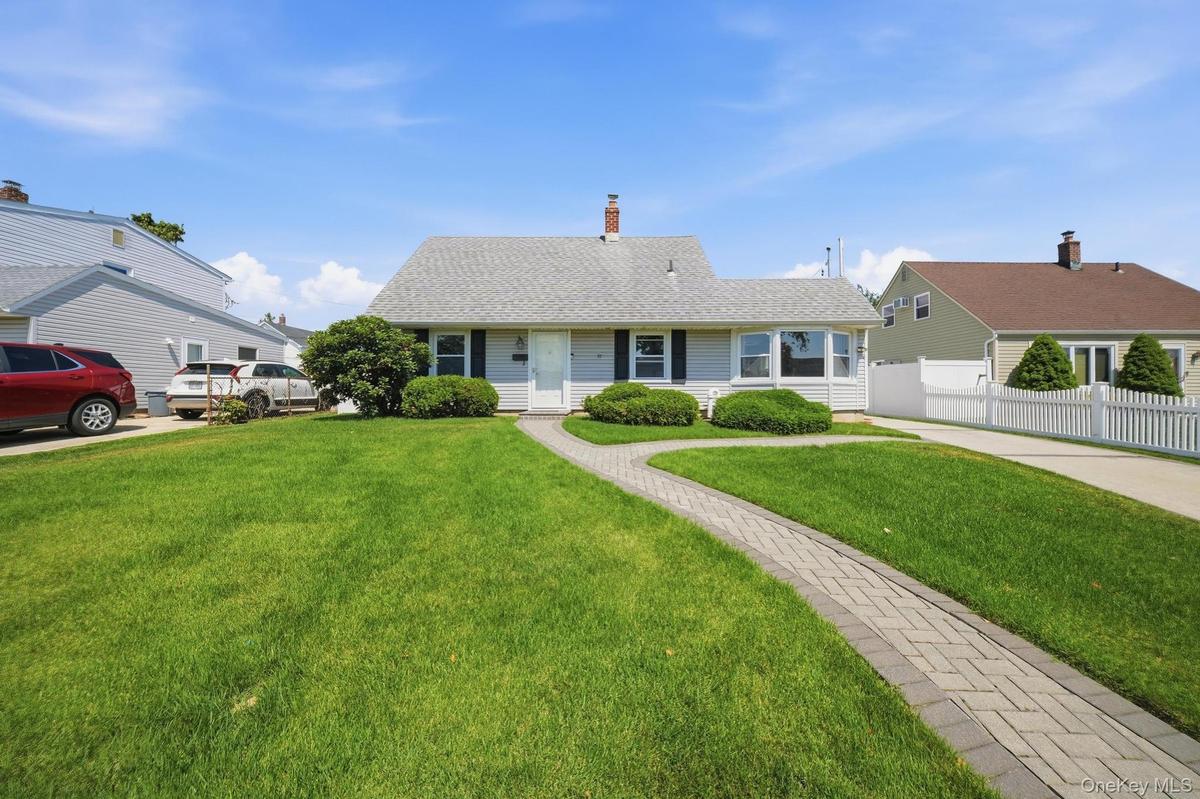 Charming ranch-style residence featuring a light gray exterior, a paved driveway, and a white picket fence
