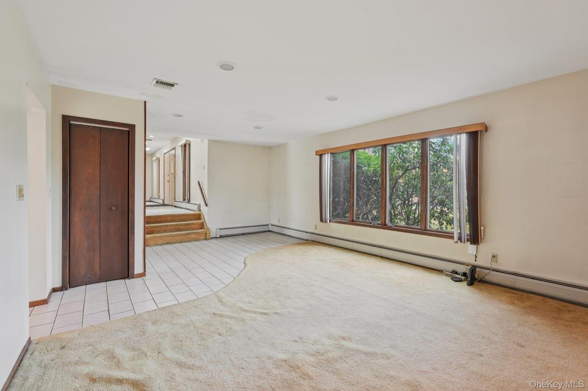 Spare room with light tile patterned floors, light colored carpet, a baseboard heating unit, stairs, and recessed lighting