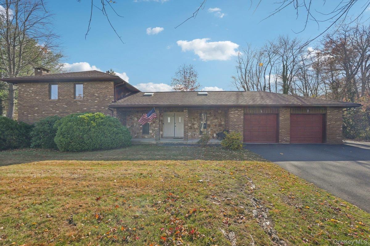 View of front of property with a garage, driveway, brick siding, a front lawn, and a chimney