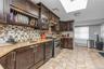 Kitchen featuring dark brown cabinetry, glass insert cabinets, light stone counters, tasteful backsplash, and range with two ovens