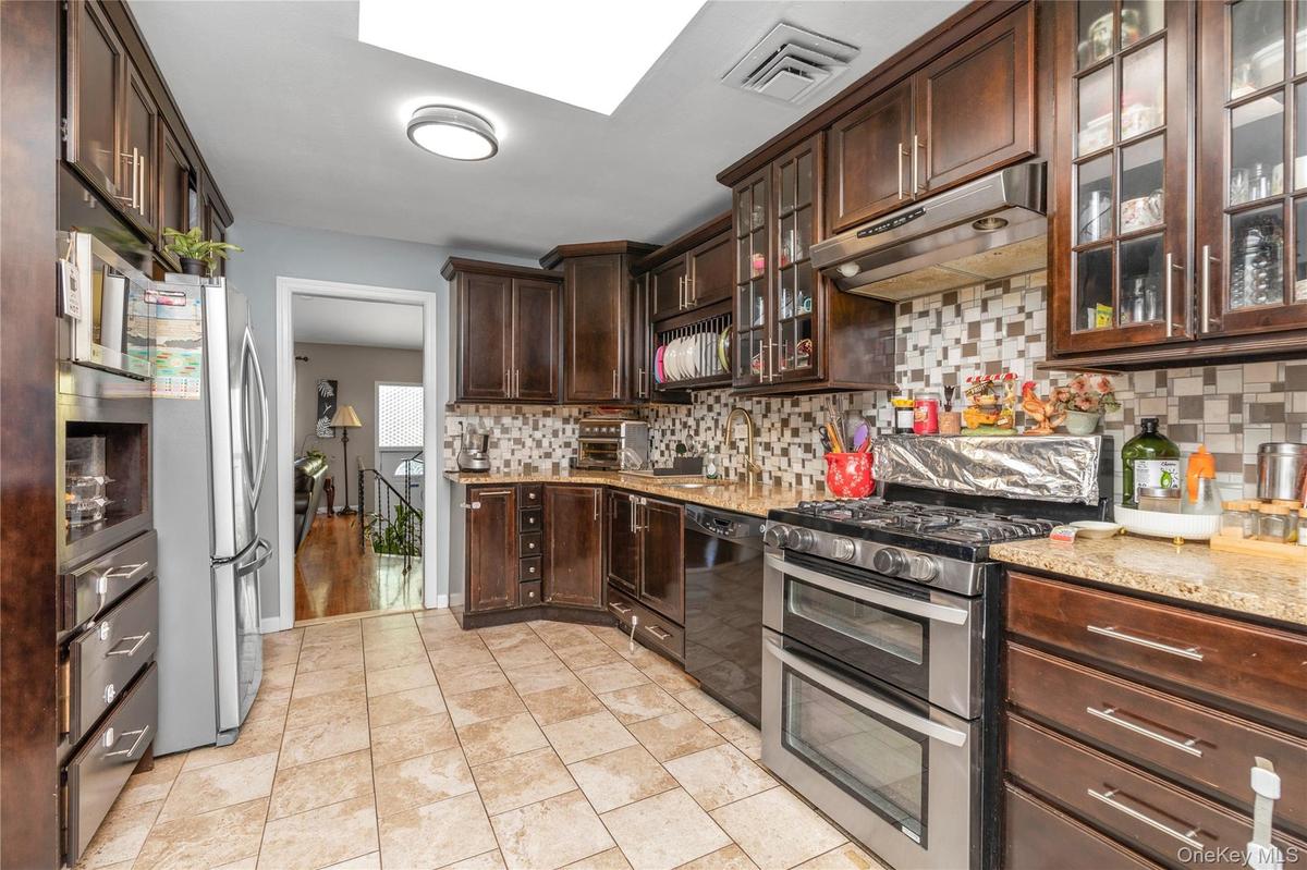Kitchen featuring backsplash, stainless steel appliances, dark brown cabinetry, under cabinet range hood, and glass insert cabinets