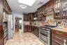 Kitchen featuring backsplash, stainless steel appliances, dark brown cabinetry, under cabinet range hood, and glass insert cabinets