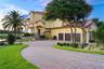 A winding paver drive framed by towering palms and manicured grounds creates a grand arrival, setting the stage for this remarkable waterfront estate 
