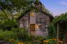 As evening falls, the wellness studio glows warmly amid mature gardens and lush landscaping