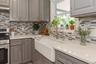 Modern kitchen featuring a white farmhouse-style sink, light gray cabinetry, stainless steel appliances, a mosaic tile backsplash, and light-colored c