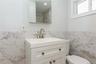 White vanity with integrated sink, brushed nickel faucet, wall-mounted mirror, and white tiled half-wall with gray veining