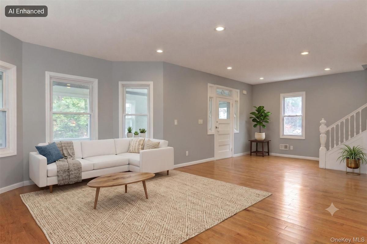 Open-concept living area featuring hardwood flooring, recessed lighting, multiple windows, a bay window, and a white staircase with balusters (virtual