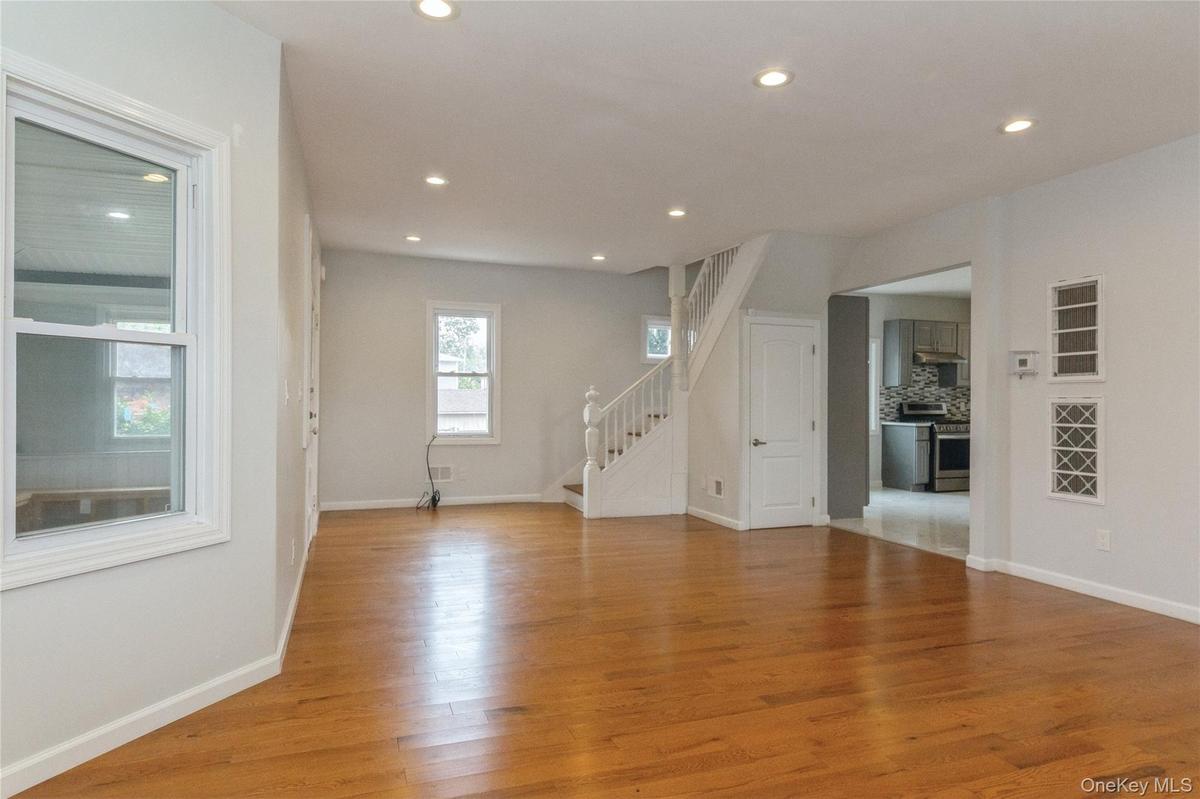 Expansive living area featuring warm wood-finish flooring, recessed lighting, white trim, and a staircase with white balusters