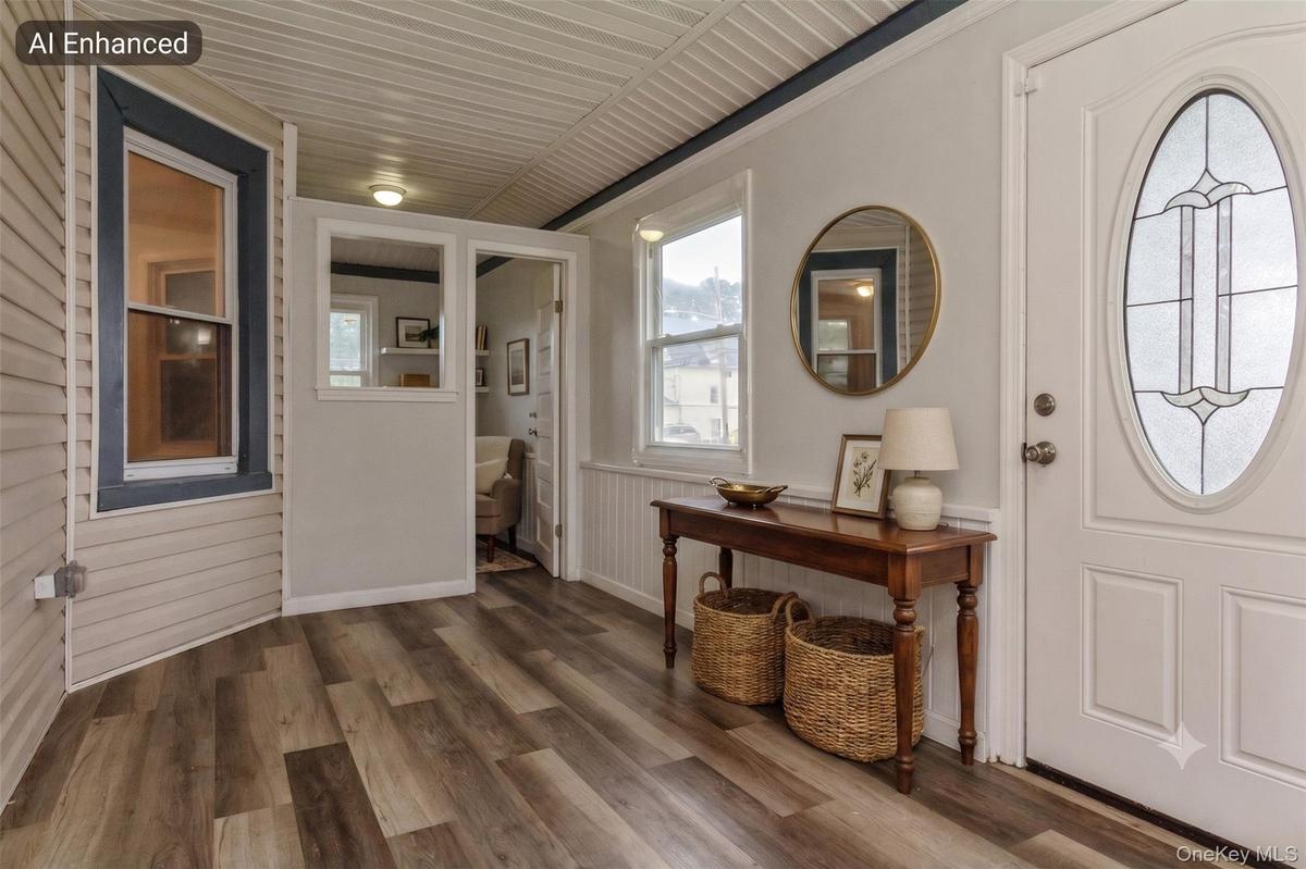 Entryway featuring a white paneled door with an oval stained-glass insert, wood-finish flooring, and white beadboard wainscoting(virtually staged)