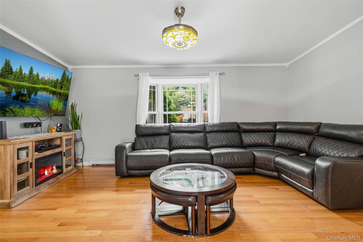 Living area featuring wood-finish flooring, a bay window with natural light, light gray wall paint, and white crown molding