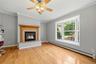 Living area featuring a gas fireplace with a wood mantle and stone surround, a bay window, wood-finish flooring, and crown molding