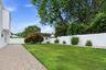 Expansive backyard featuring a paver patio, manicured lawn, white privacy fence, and mature landscaping