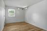 Room featuring wood-finish flooring, white painted walls, a single window with blinds, a baseboard heater, and ceiling-mounted track lighting