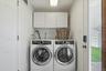Dedicated laundry area featuring front-loading washer and dryer, upper cabinetry for storage, and a white paneled door