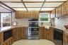 Kitchen featuring wood cabinetry, light-toned tiled backsplash, granite-finish countertops, and a full suite of appliances including a double oven ran