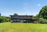 Contemporary style residence featuring a dark brown exterior, an expansive upper-level deck with wooden railings, and a lower-level patio with double 