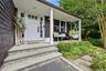 Welcoming front entry featuring a white paneled door with sidelights, a covered porch with white columns, stone steps, dark-stained cedar shake siding